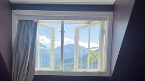 Un dormitorio con cama, almohadas, una ventana con cortinas y vistas a montañas.