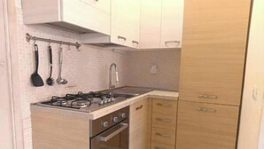 Eine kleine Küche mit Gaskochfeld, Backofen und Spüle. Es gibt Holzschränke mit silbernen Griffen und eine geflieste Spritzschutzwand.