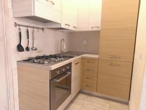 Eine kleine Küche mit Gaskochfeld, Backofen und Spüle. Es gibt Holzschränke mit silbernen Griffen und eine geflieste Spritzschutzwand.