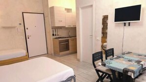 Ein gemütlicher Raum mit Bett, Esstisch mit Stühlen, einer kleinen Küche und einem an der Wand befestigten Fernseher.