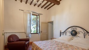 A bedroom with a bed, a chair, a radiator, a window with curtains, and a door. - Holiday Home 'Il Granaio' with Shared Garden and Wi-Fi (Arezzo)