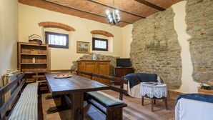 A rustic room with a wooden table, benches, a sofa, a small table with a lace tablecloth, and a stone wall. - Holiday Home 'Il Granaio' with Shared Garden and Wi-Fi (Arezzo)
