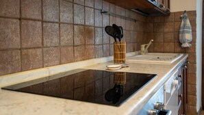 A kitchen with a black induction cooktop, a wooden utensil holder, and a hanging cloth. - Holiday Home 'Il Granaio' with Shared Garden and Wi-Fi (Arezzo)