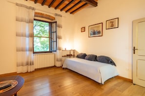 A bedroom with a bed, wooden floor, window with curtains, radiator, and a door. - Country House 'Il Nido' with Shared Garden and Wi-Fi (Arezzo)