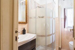 Ein Badezimmer mit einer gläsernen Duschkabine, einem weißen Waschbecken und einem Spiegel mit goldener Rahmung.