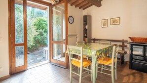 Un coin repas avec une table et des chaises, une horloge au mur et une vue sur l’extérieur à travers une porte vitrée.