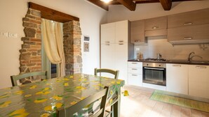 Une cuisine avec des armoires blanches, un four encastré et une cuisinière. On y trouve une table à manger avec des chaises et un mur en pierre.