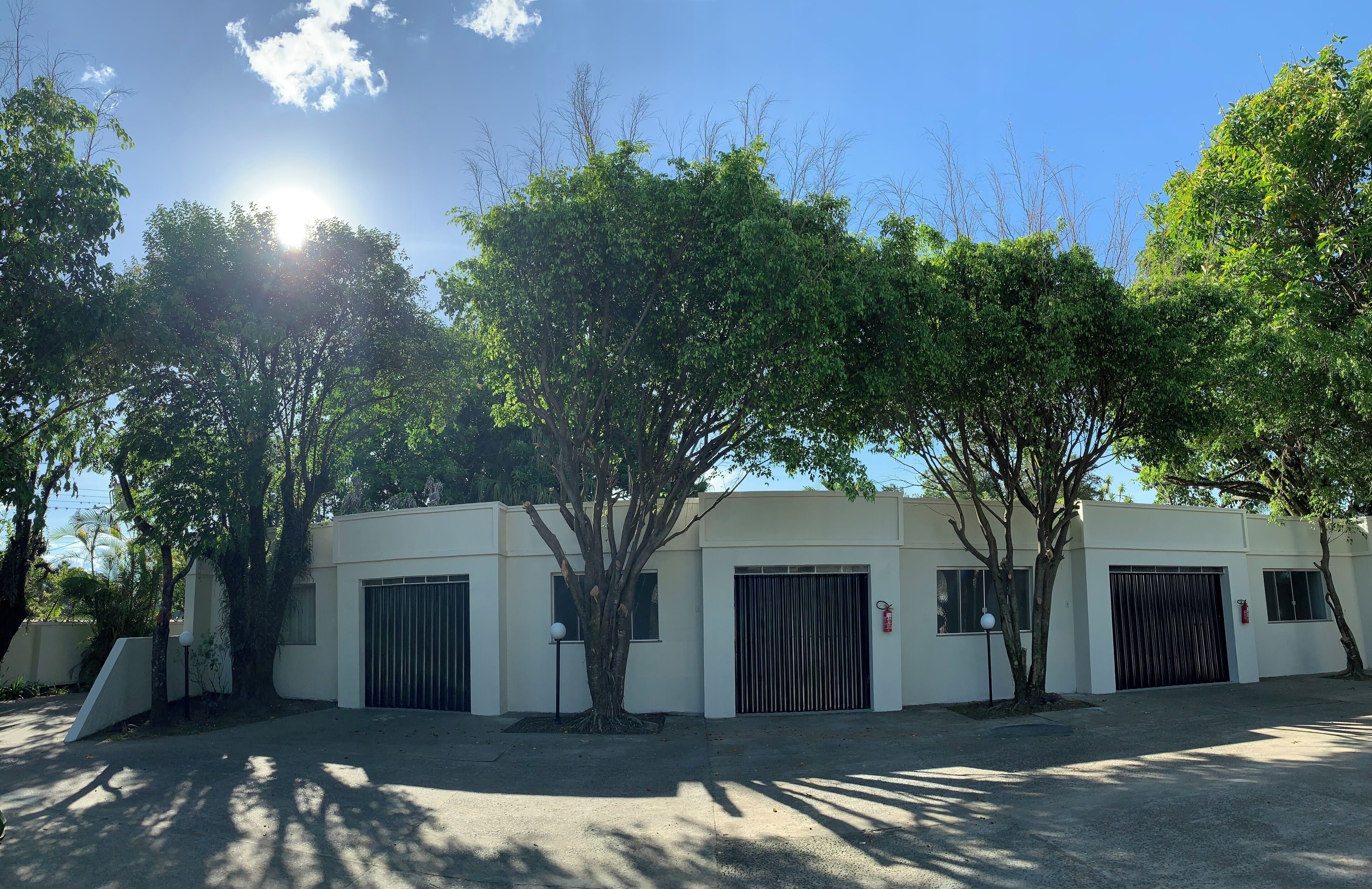 A building with a white exterior, multiple garage doors, and trees in front.