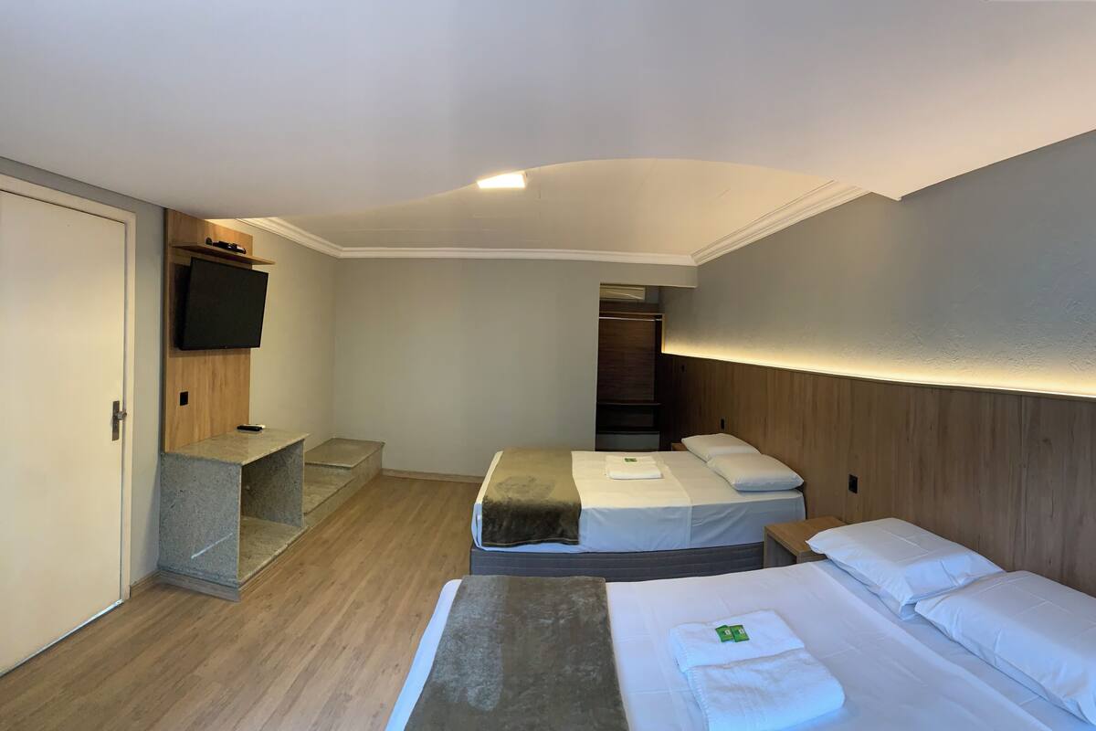 A hotel room with two beds, a TV, a wooden headboard, a small desk, and a closet.