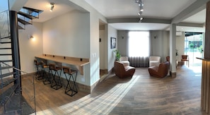Un intĂ©rieur moderne avec un escalier, un coin bar, des siĂšges et une grande fenĂȘtre.