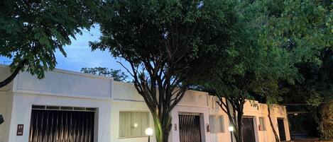Un edificio con una entrada protegida por una reja, un árbol en primer plano y un cielo despejado.