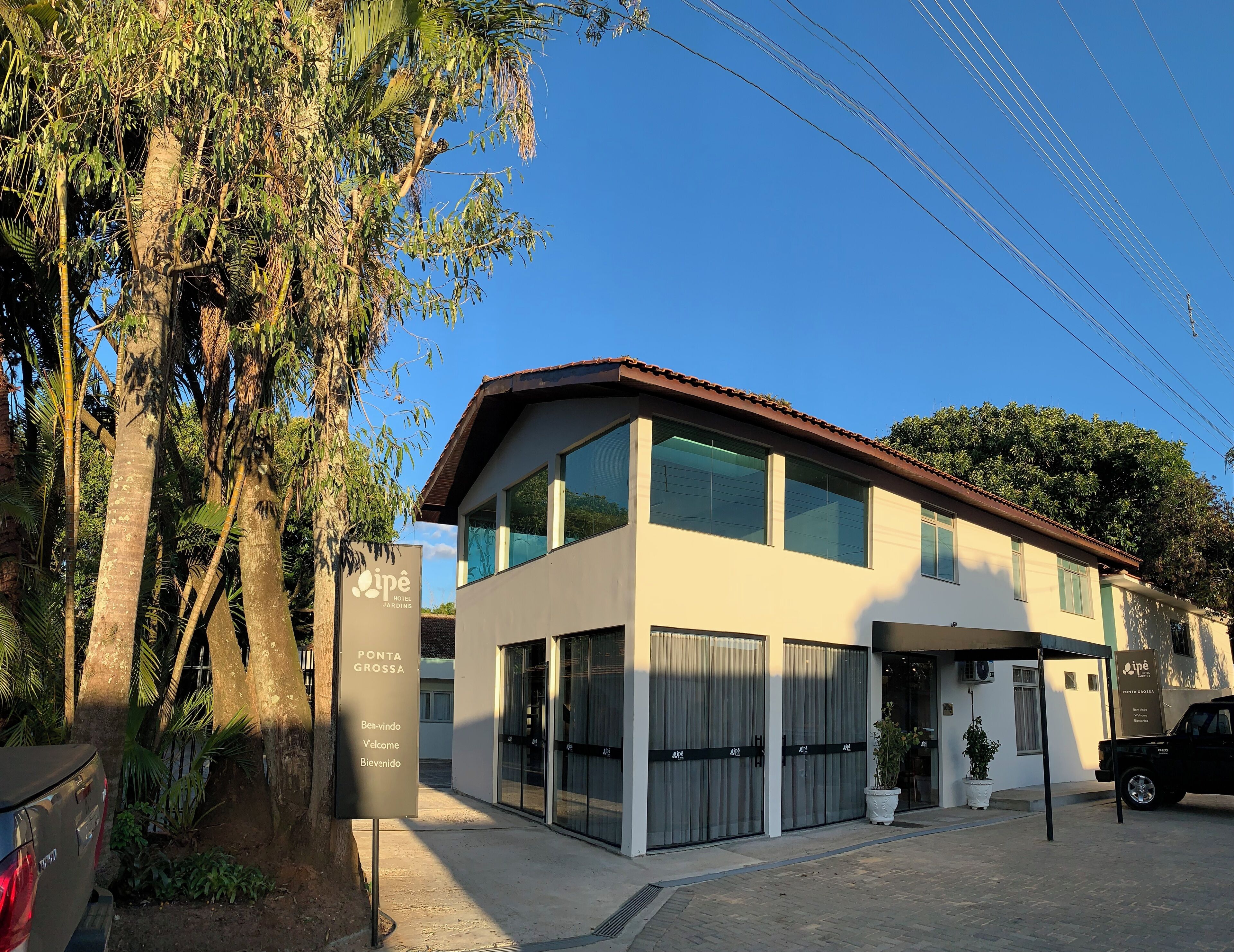 A modern hotel with a two-story structure, large windows, and a sign indicating 'Ponta Grossa' and 'Ben-vindo Veloce.'