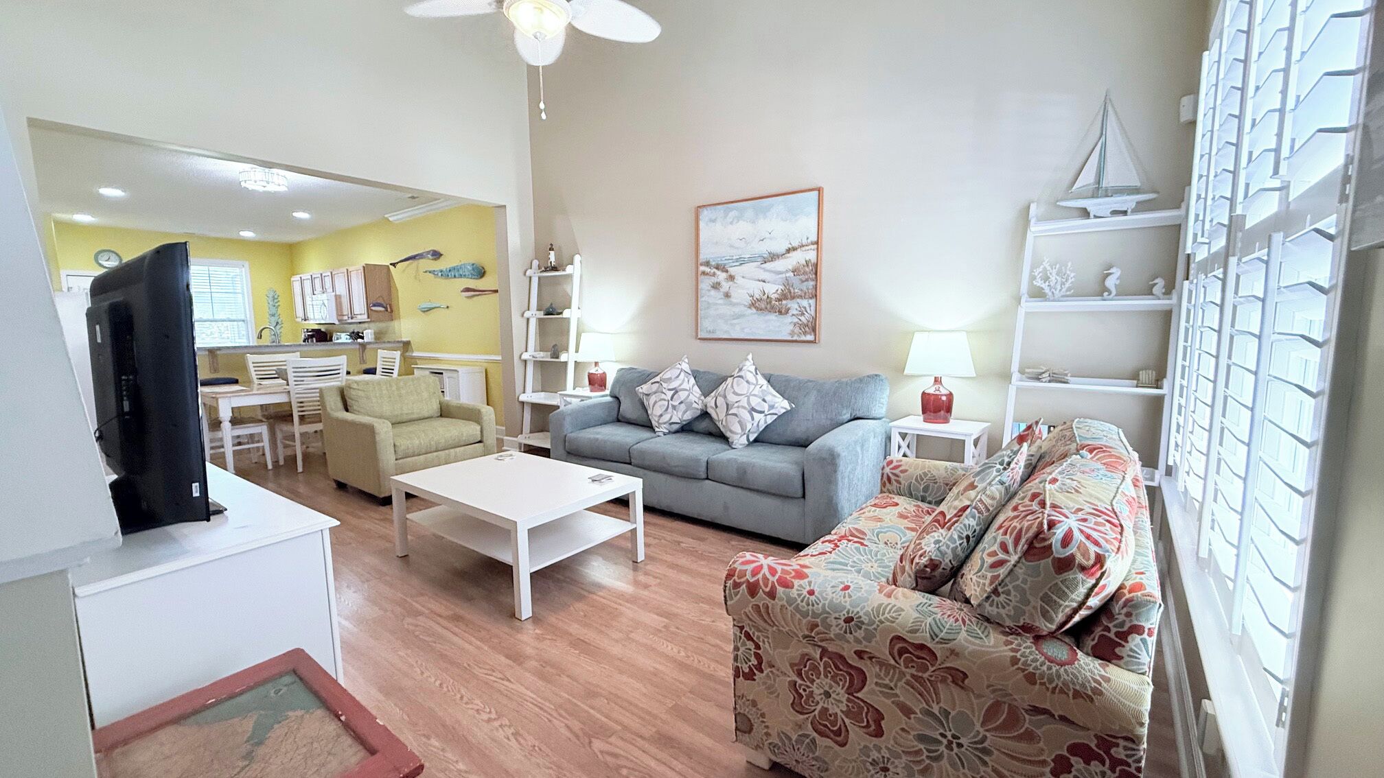 Uma sala de estar com sofá, mesa de centro, televisão e um quadro na parede.