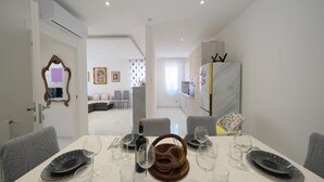 A modern dining area with a white table set for six, a kitchen in the background, and a living area with a sofa and chairs. - Seaside Apartment - Sleeps 6 - Balcony (Rapallo)