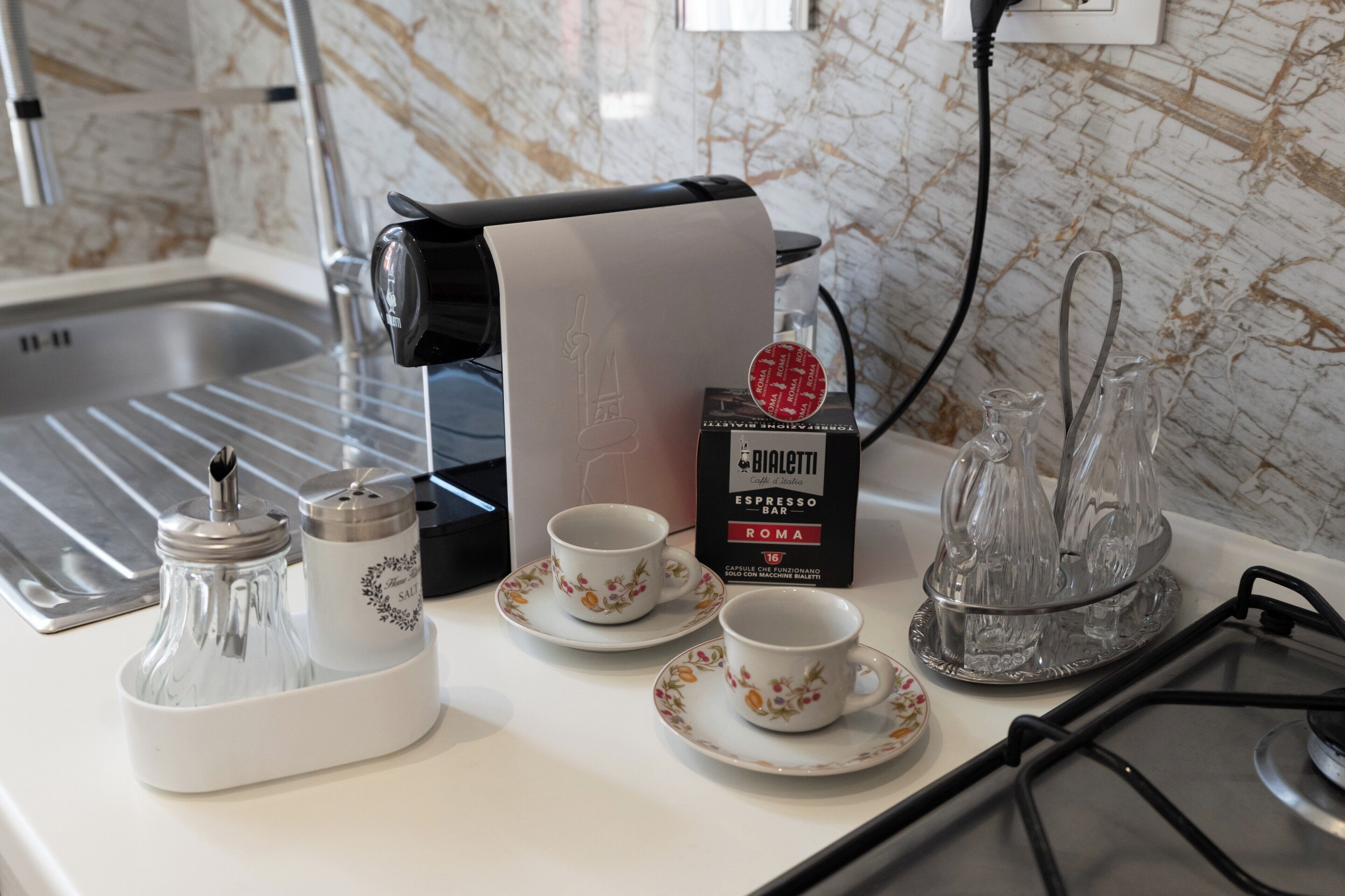Una encimera de cocina con una cafetera, dos tazas, un salero y pimentero, una jarra de vidrio y una caja de espresso bar Bialetti.