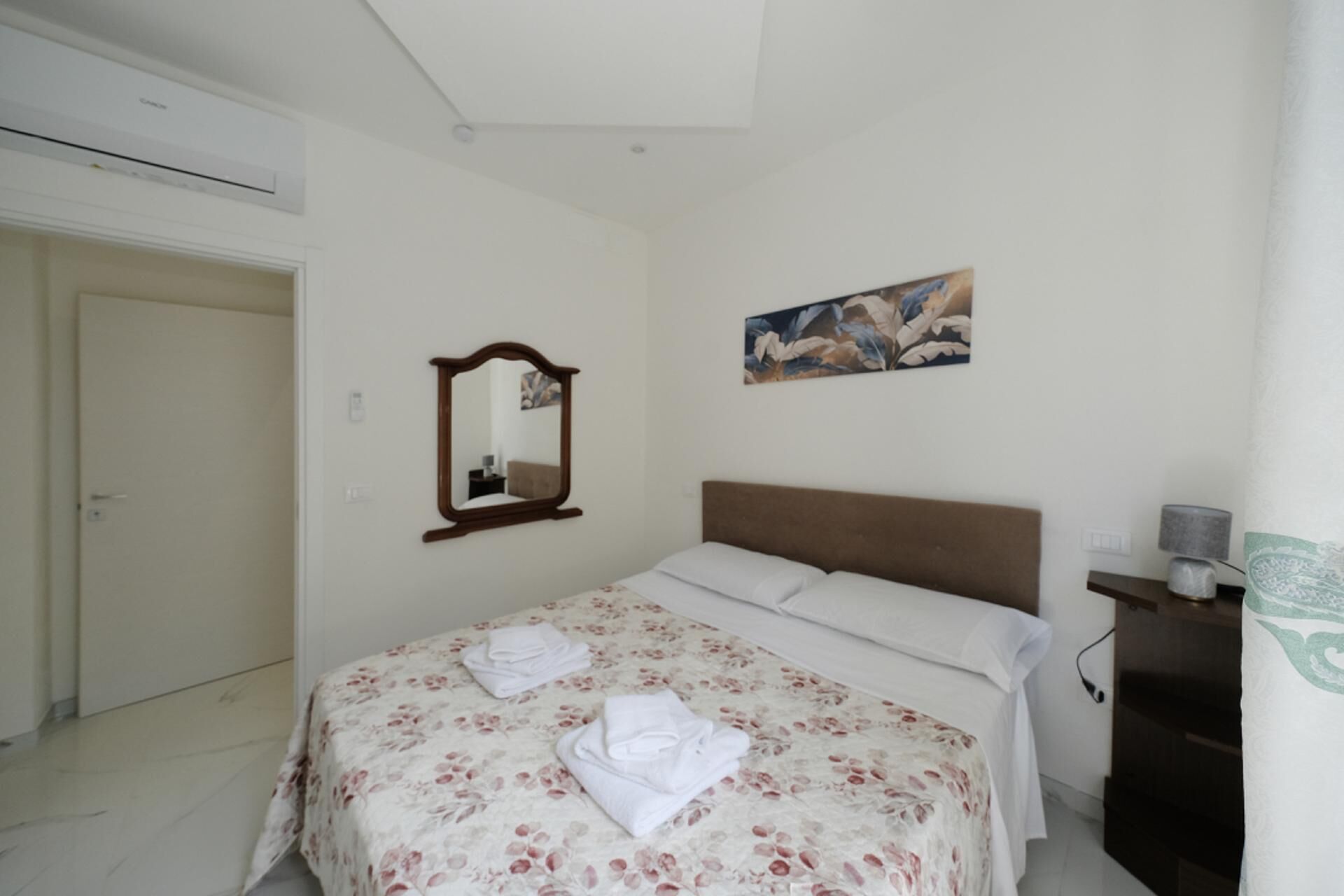 Une chambre à coucher avec un lit, un miroir, un tableau, une porte et une commode.