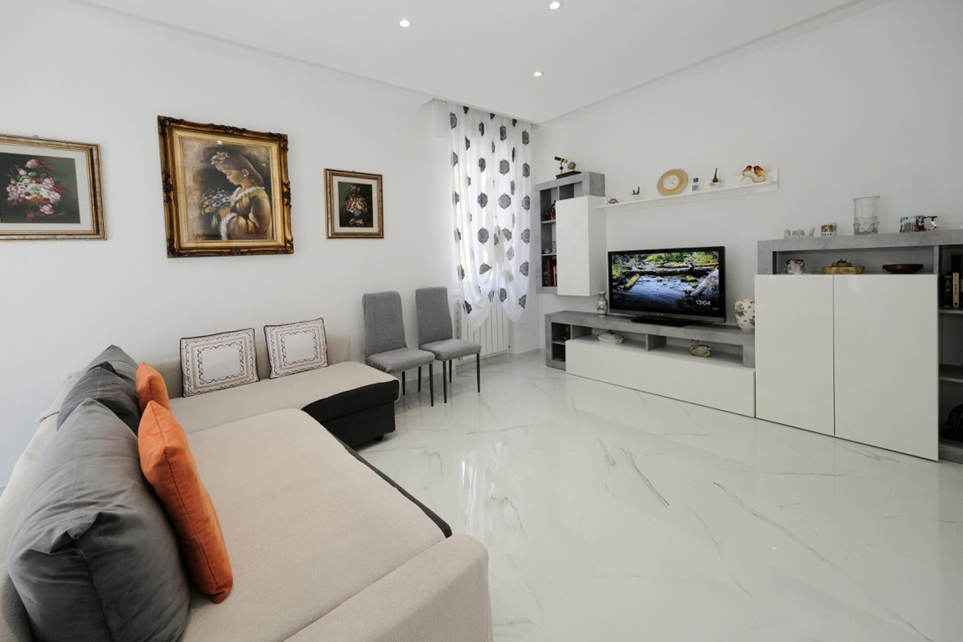 Uma sala de estar moderna com sofá, cadeiras, televisão e quadros na parede.