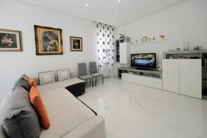A modern living room with a sofa, chairs, a TV, and framed artwork on the wall. - Seaside Apartment - Sleeps 6 - Balcony (Rapallo)