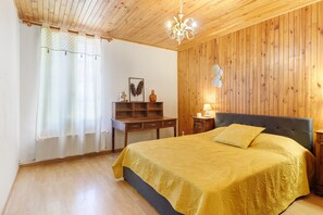 Ein Schlafzimmer mit Holzbalkendecke, einem Bett mit gelber Bettdecke, einem Nachttisch mit Lampe und einer Kommode mit Dekorationen.