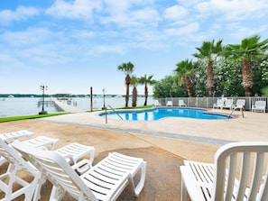 A pool with lounge chairs, palm trees, and a view of the water. - The Landing Gulf Shores #104 | Beach + Lagoon Access + Pool (Gulf Shores)