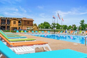 A swimming pool with lounge chairs, a wooden building, and flags. - The Landing Pad – Stylish 2BR Condo Steps from Branson Landing, Dining & Entertainment (Branson)