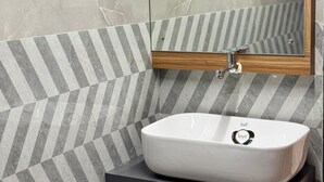 A bathroom with a white sink, a mirror, and a geometric-patterned wall. - Yatri Stay inn (Mumbai)