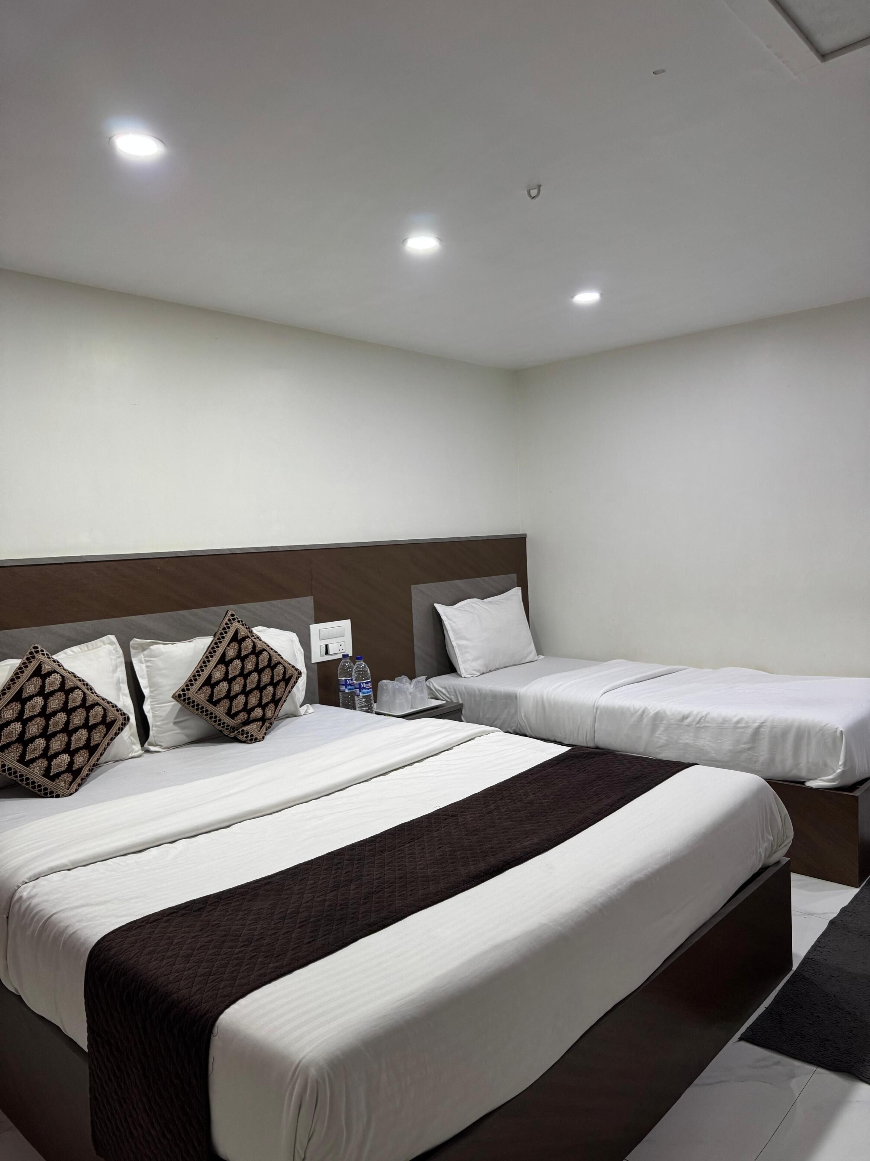 Ein Hotelzimmer mit zwei Betten, einem Kopfteil und einem Nachttisch mit Wasserflaschen.