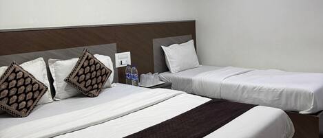 Ein Hotelzimmer mit zwei Betten, einem Kopfteil und einem Nachttisch mit Wasserflaschen.