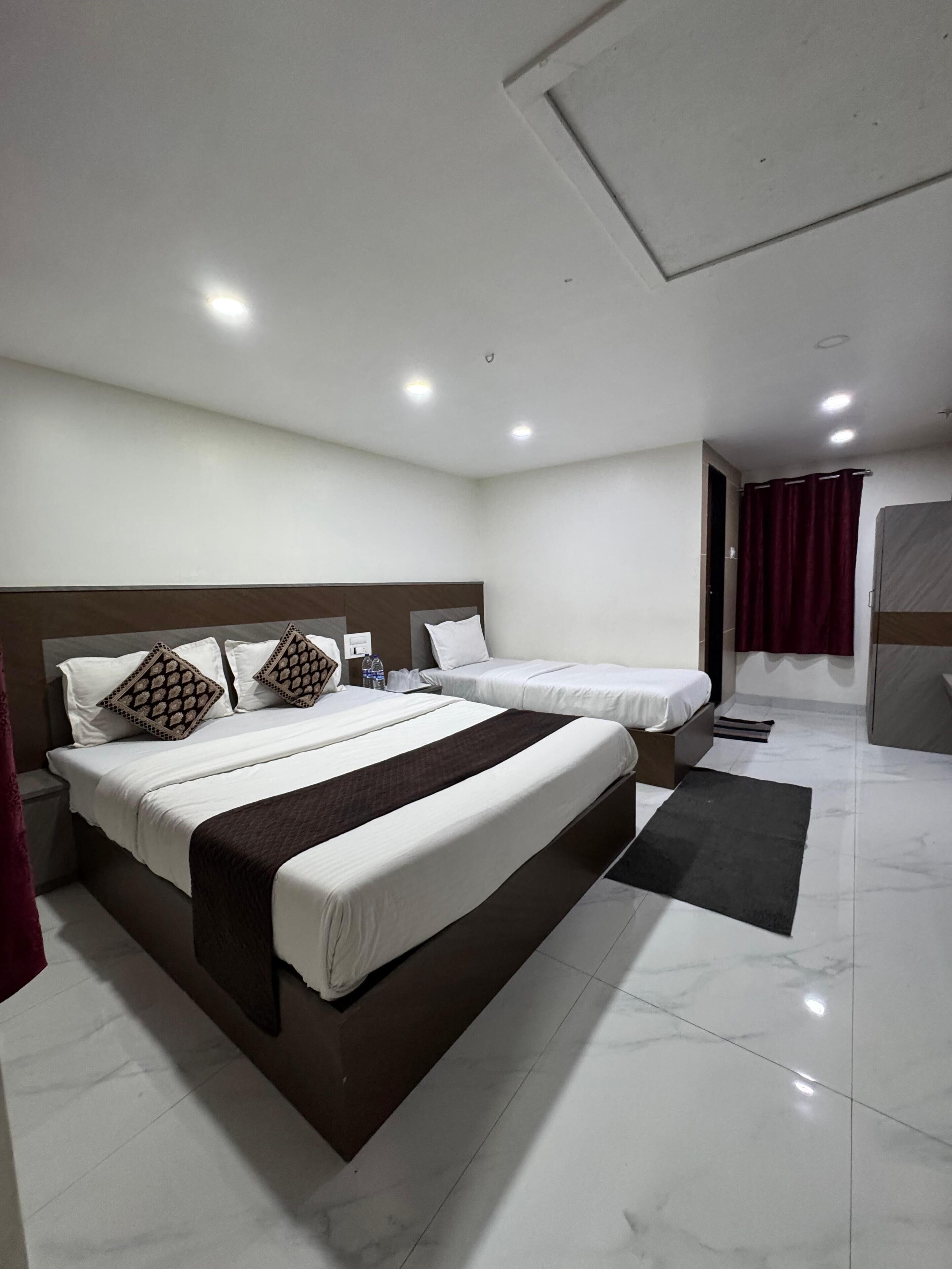 A modern hotel room with a large bed, a smaller bed, a bathroom, and a shower area.