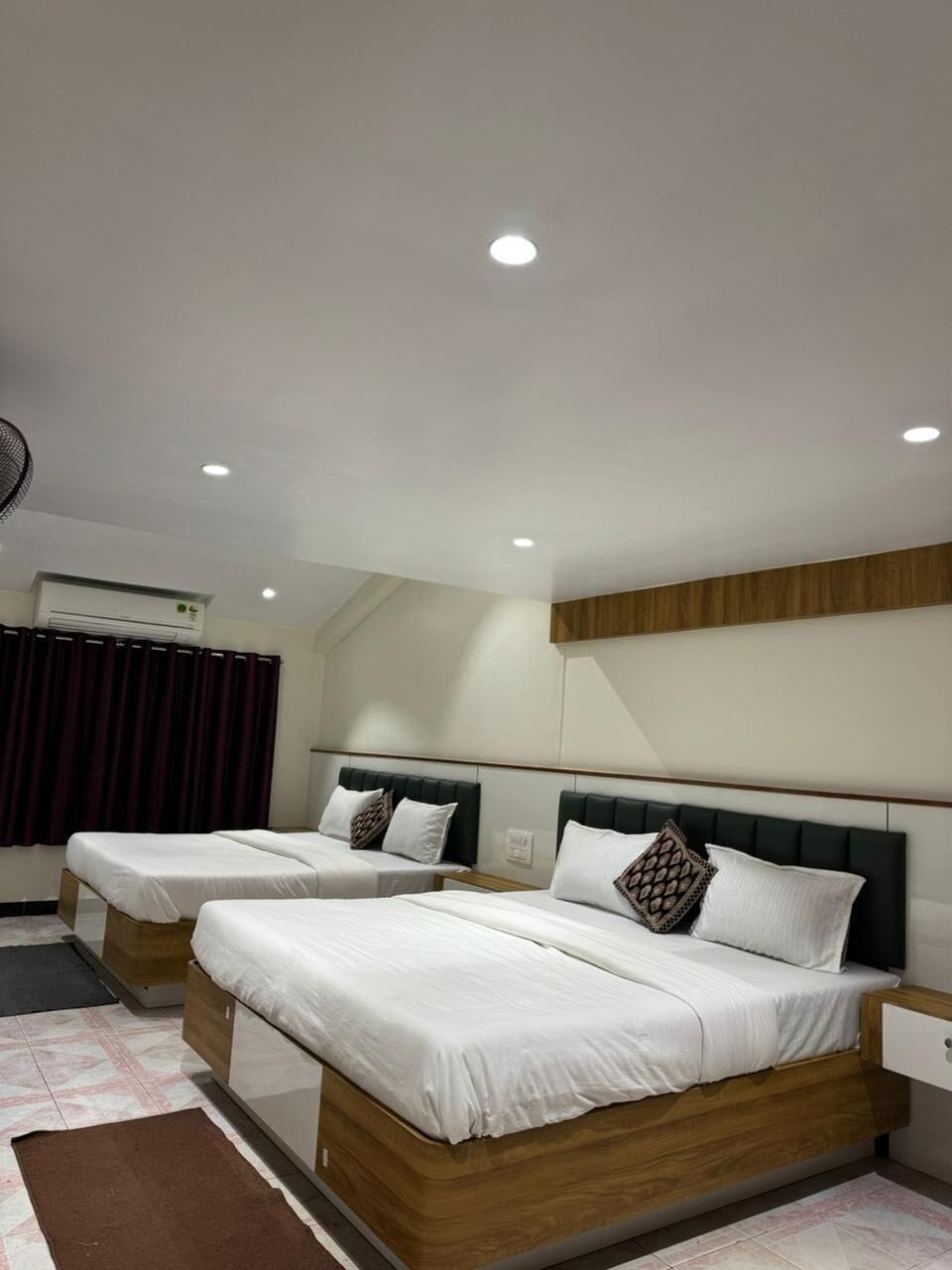 A hotel room with two beds, a ceiling fan, an air conditioning unit, and a wooden headboard.