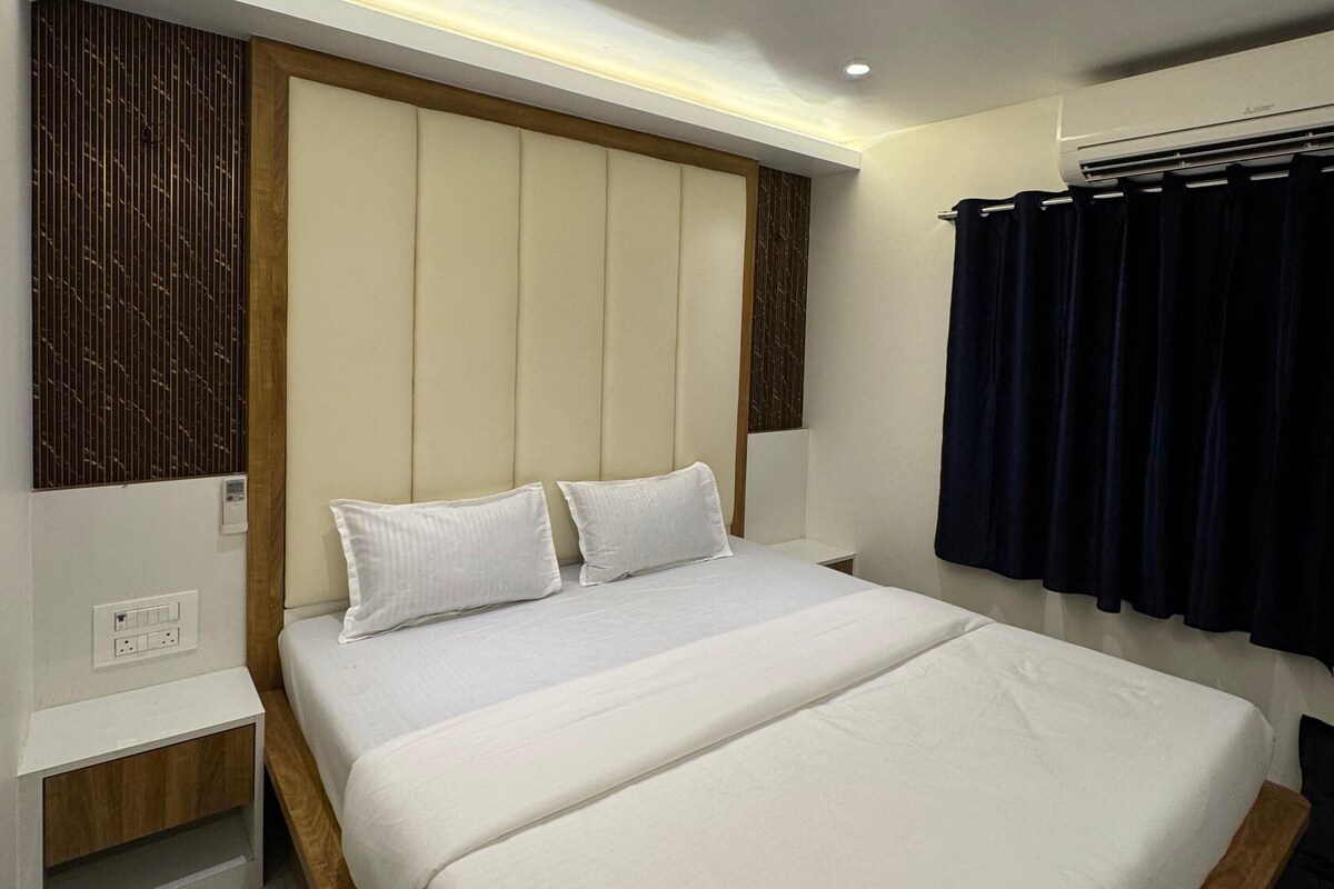 Una habitación de hotel moderna con una cama grande, una mesita de noche, un equipo de aire acondicionado y una cortina oscura.