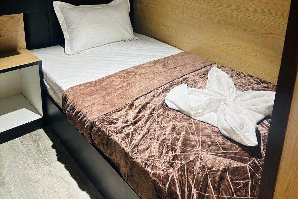 Una cama individual con un almohadón blanco, una manta marrón y una toalla blanca en el suelo.