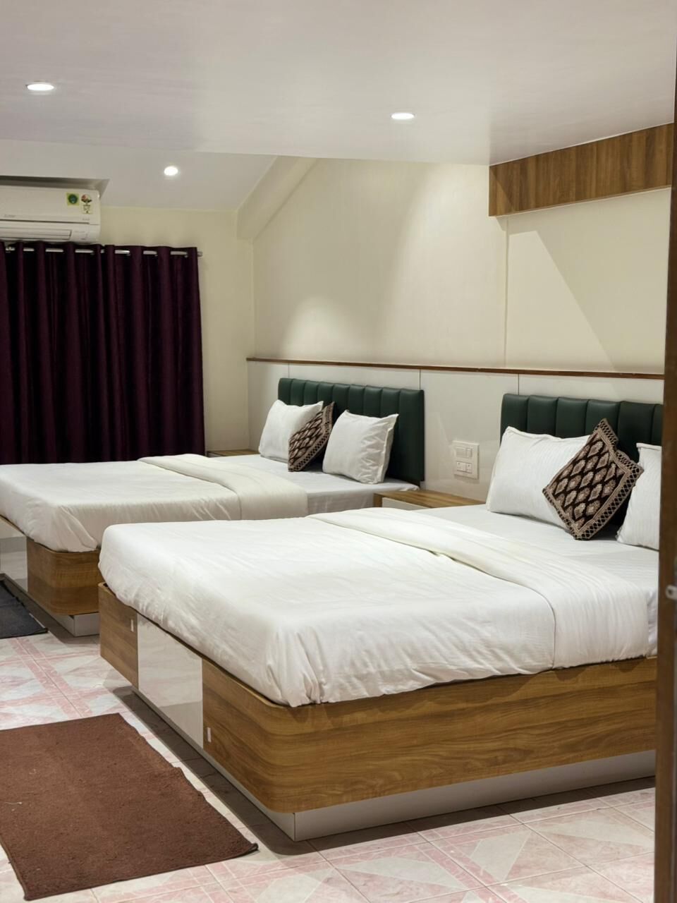 Una habitación de hotel con dos camas individuales, un cabecero de madera, un tapete marrón y un equipo de aire acondicionado.