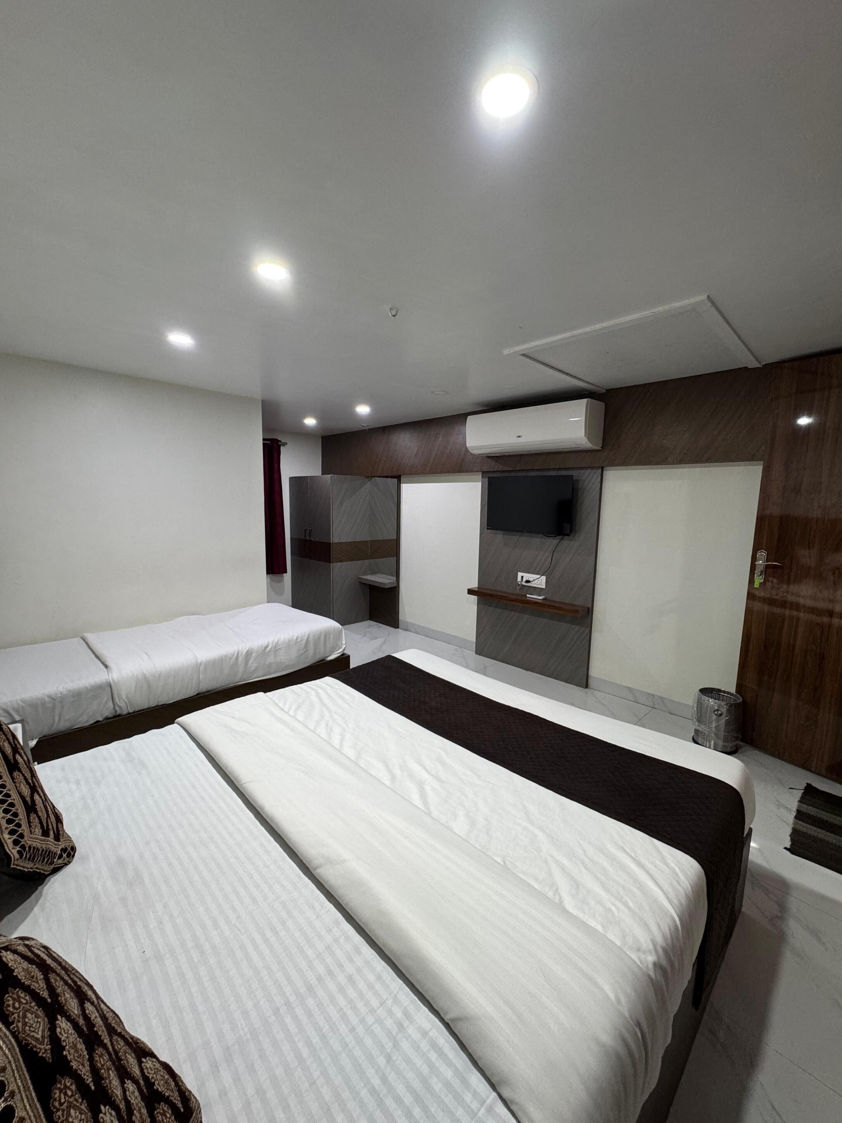 A hotel room with two beds, a TV, an air conditioning unit, and a wooden panel wall.