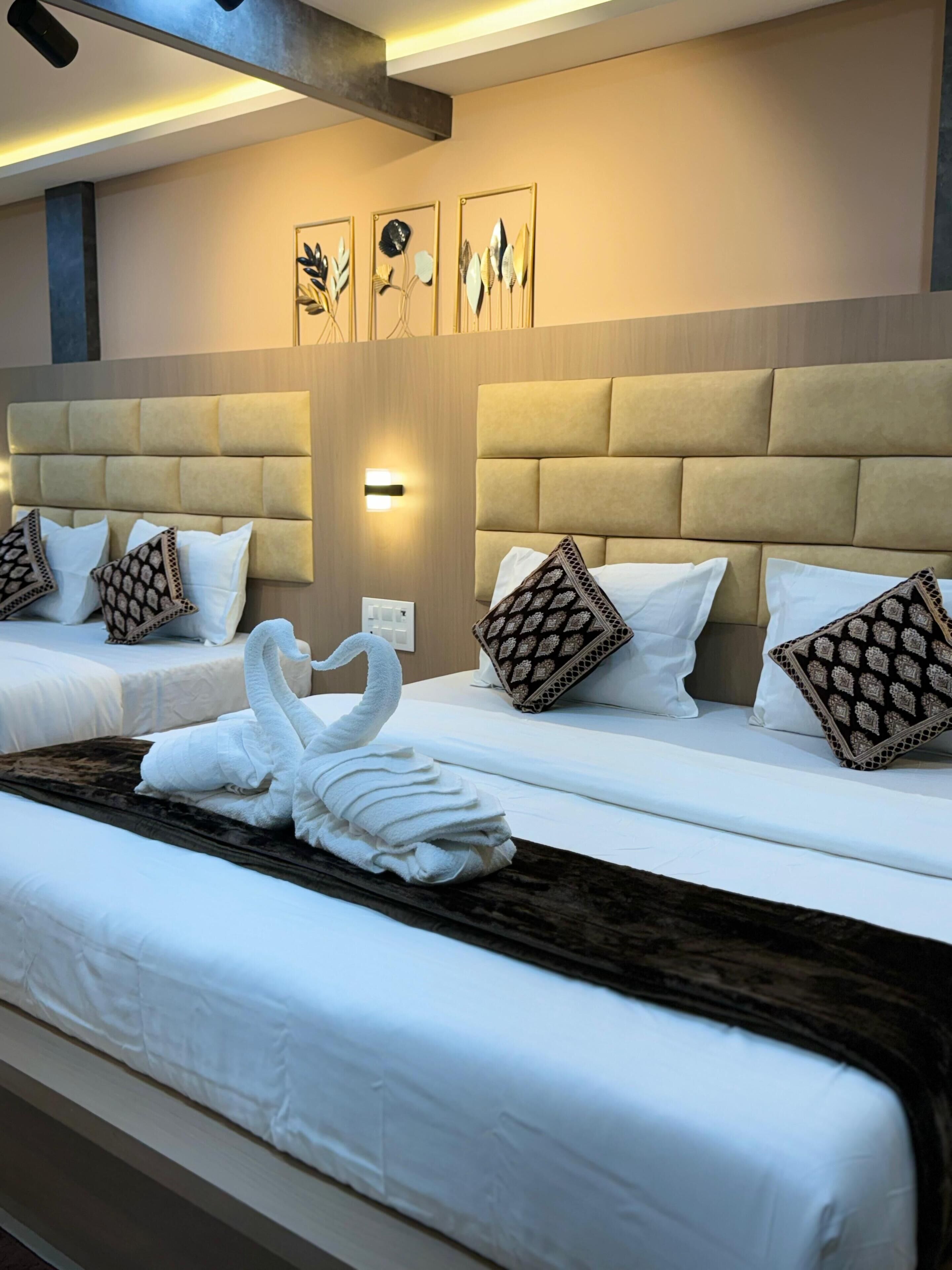 Habitación de hotel con dos camas, cabecero, decoración en la pared y una escultura de toalla con forma de cisne.