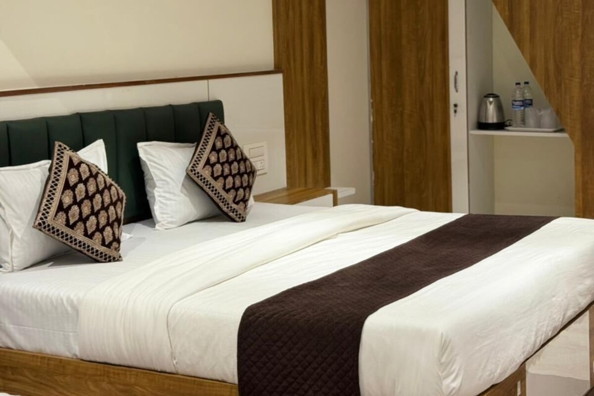 Una habitación de hotel moderna con una cama, cabecera de madera, un escritorio pequeño con una silla y un armario.