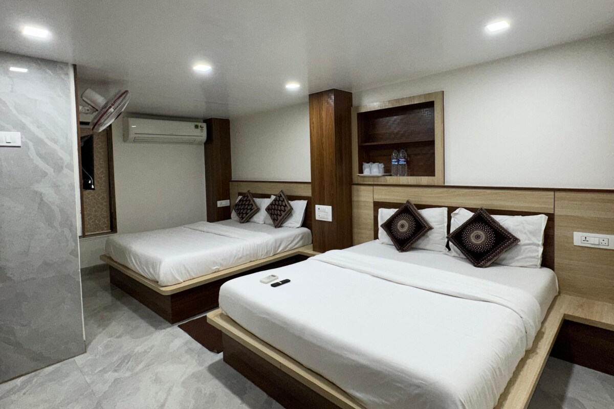 Habitación de hotel con dos camas, cabecera de madera, repisa con botellas y ventilador de techo.