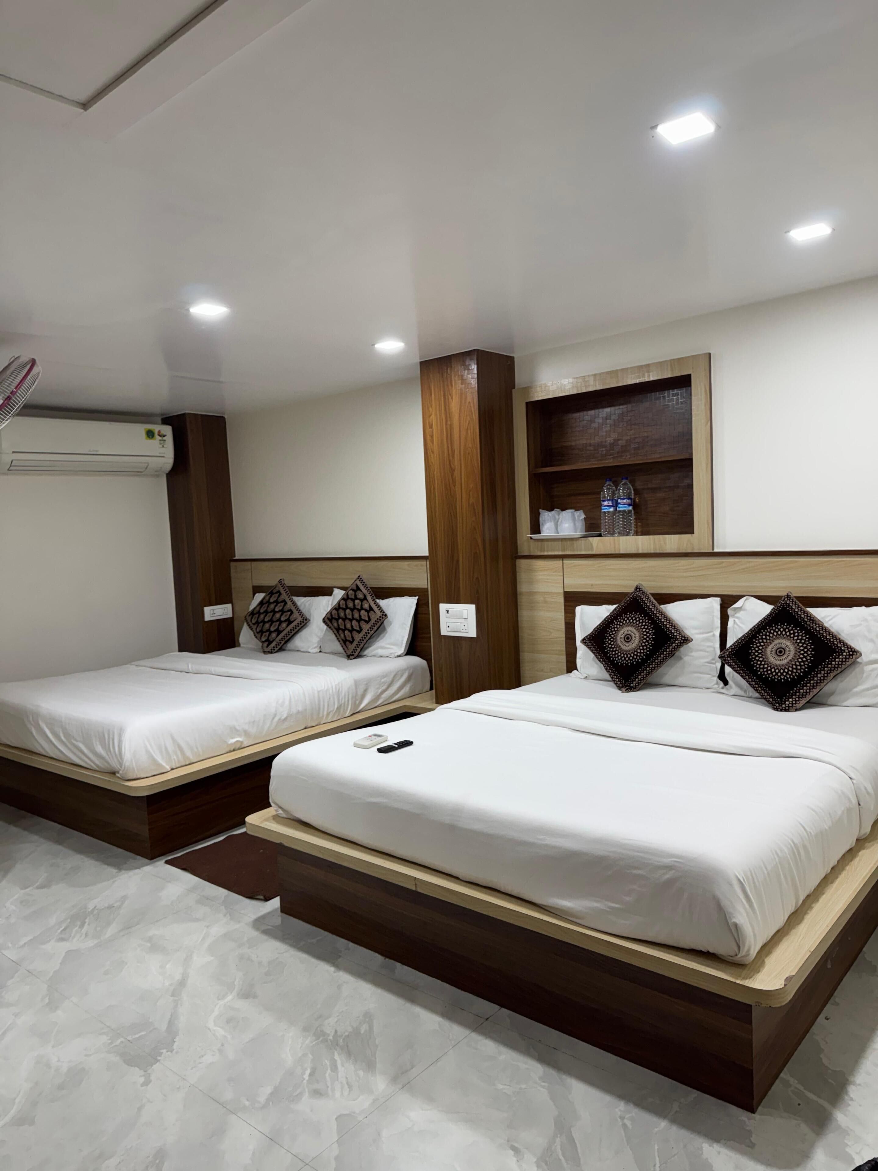 Two single beds with wooden headboards, a built-in shelf with water bottles, and an air conditioning unit on the wall.