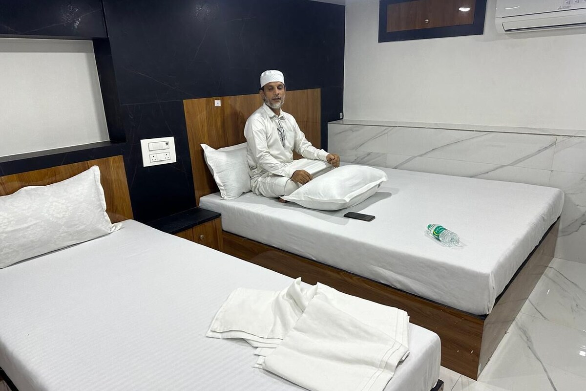 Habitación de hotel con dos camas, cabecero de madera, mesita de noche y aire acondicionado de pared.
