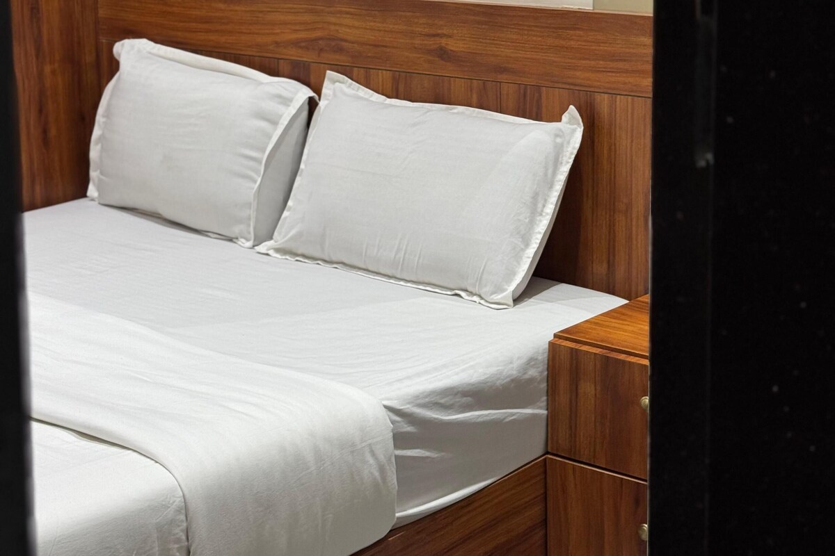 Un dormitorio con cabecera de madera, una cama con ropa blanca y una mesita de noche con cajones.