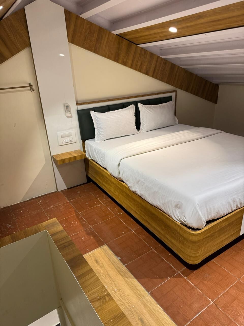 Een slaapkamer met een bed, een houten hoofdbord, witte beddengoed, een nachtkastje en een stopcontact.