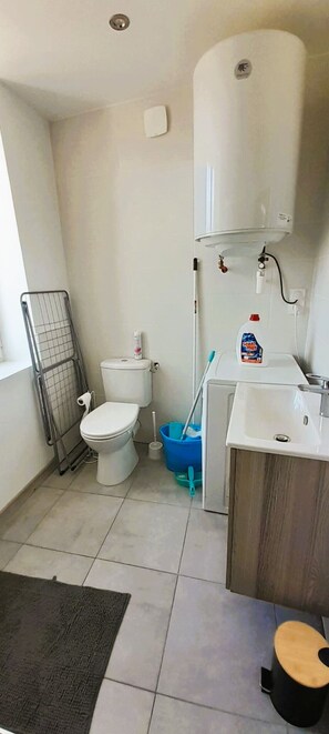 Une petite salle de bain comprenant des toilettes, un lavabo et un chauffe-eau fixé au mur.