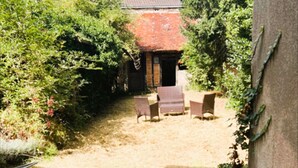 Une cour bordée d’un mur de briques, un petit bâtiment avec un toit rouge et un espace aménagé avec des chaises.