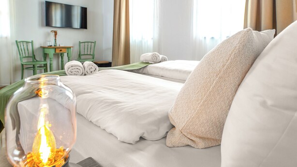 A hotel room with two beds, a TV mounted on the wall, a small table with chairs, and a large vase with a light.