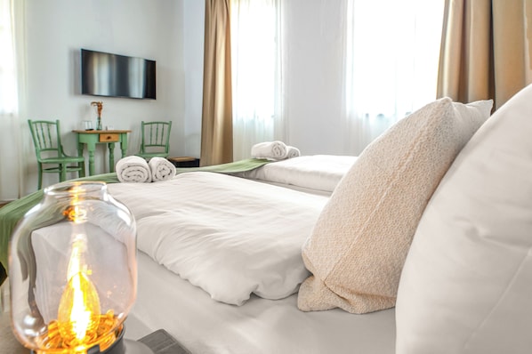 Habitación de hotel con dos camas, un televisor montado en la pared, una mesita con sillas y un jarrón grande con luz.
