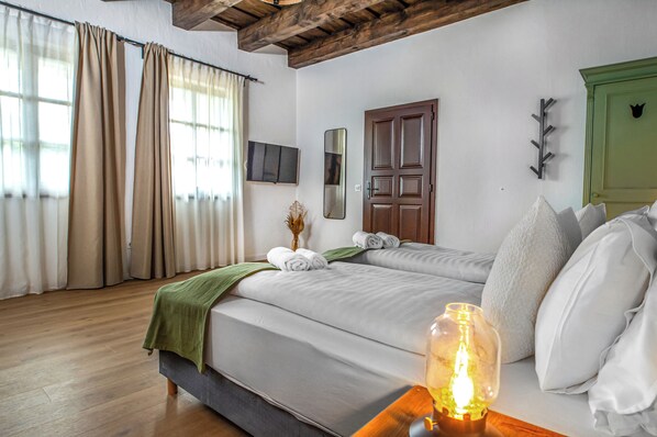 Habitación de hotel con dos camas, techo de madera, puerta verde y una mesita de noche con lámpara.