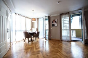 A spacious room with a wooden herringbone floor, a dining table with chairs, a pendant light, and a sliding glass door leading to a balcony. - Lux central 1,5 bedroom apartment (Berlin)