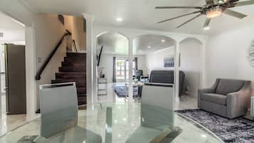 A modern living room with a glass-top dining table, a gray sofa, and a ceiling fan.