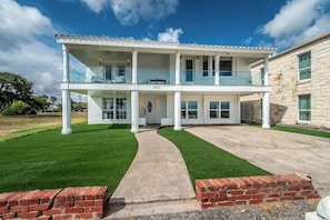 A two-story house with a covered front porch, a driveway, and a well-maintained lawn. - Ocean Drive Splendor Awaits (Corpus Christi)