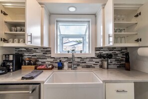 A modern kitchen with a central island, a window above the sink, and a backsplash with rectangular tiles. - Ocean Drive Splendor Awaits (Corpus Christi)